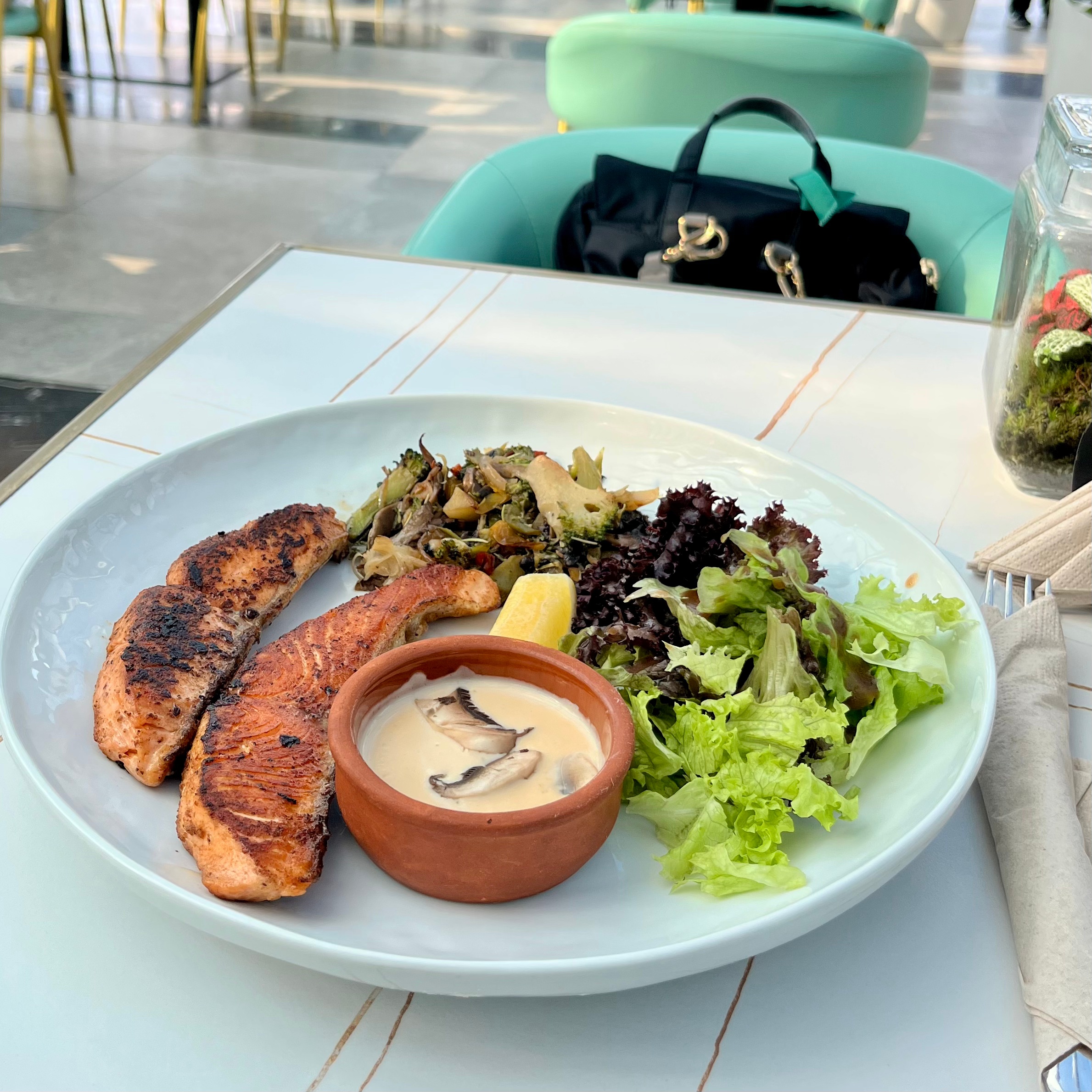 A sky blue plate with grilled salmon, mushroom sauce and a side of vegetables.